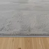 A close-up view of a fluffy gray rug on a wooden floor. Voir les images du produit