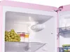Interior view of a pink retro refrigerator, showing food items on shelves. Produktbild-Vorschau
