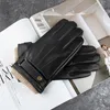 A pair of black leather gloves with tan knit cuffs are placed on an open magazine. Produktbild-Vorschau