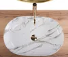 A top-down view of a marble-patterned sink with a gold faucet, placed on a wooden surface. Anteprima dell’immagine prodotto