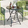 A round glass-top bistro table with two green woven chairs on a tiled patio. Anteprima dell’immagine prodotto