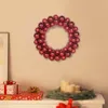 A red Christmas ball wreath is hung on a wall above a white dresser decorated with Christmas gifts and candles. Produktbild-Vorschau