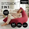 A woman is sitting on a large red beanbag chair in a modern living room with a sectional sofa in the background. Voir les images du produit