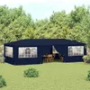 A navy blue party tent set up in a grassy backyard with trees in the background. There is outdoor furniture inside the tent. Voir les images du produit