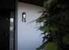 A close-up shot of a modern outdoor wall light mounted on a white brick wall next to a dark door. Anteprima dell’immagine prodotto