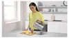 A woman is pouring hot water from a kettle into a glass with fruit and ice. Produktbild-Vorschau