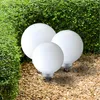 Three white globe lights are placed on a gravel path in front of a green hedge. Produktbild-Vorschau