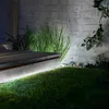 A close-up of a wooden deck with integrated LED lighting, surrounded by grass and a brick wall. Produktbild-Vorschau