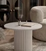 A round coffee table with a ribbed base is placed on a rug in a living room. A diffuser and a book are on the table. Voir les images du produit