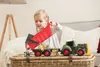 A young child is playing with a toy tractor and trailer on a woven basket. Produktbild-Vorschau