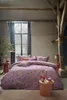 A bedroom scene with a bed dressed in floral bedding, bedside tables with decorative items, and a window in the background. Produktbild-Vorschau