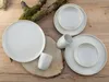 A set of white ceramic dishes and cups arranged on a wooden surface with a moss-covered branch. Náhľad obrázku produktu