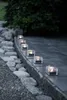 A row of solar-powered LED candles in ice cube shapes are placed along a stone pathway at dusk. Podgląd zdjęcia produktu