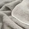 A close-up view of a soft, gray woolen blanket with a white trim. Produktbild-Vorschau