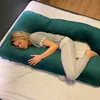 A woman is sleeping on a large U-shaped pillow in a bedroom. Náhled obrázku produktu