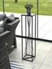 A black metal plant stand with a potted plant on top, placed on a tiled patio next to a wicker sofa. Voir les images du produit