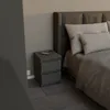 A bedside table with a remote control on top, next to a bed. Voir les images du produit