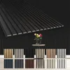 A display of various wood-look wall paneling samples against a black slatted wall background, with a vase of flowers on a small table in the midground. Produktbild-Vorschau