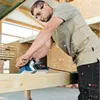 A man is using a power planer on a wooden beam in a workshop. Anteprima dell’immagine prodotto