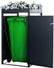 A green trash bin inside a black metal bin enclosure with a planter on top filled with blue and white flowers. Produktbild-Vorschau
