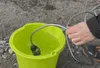 A person is holding a hose connected to a device that is submerged in a green bucket of water. Náhled obrázku produktu
