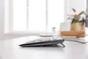A close-up side view of a black and gray CHERRY TAS STREAM KEYBOARD TKL on a white desk, with a blurred background of a window and some office plants. Náhľad obrázku produktu