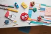 A collection of gift wrapping supplies and a gift box are arranged on a marble-like surface. Produktbild-Vorschau