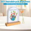 A DIY handprint frame with a colorful handprint and text on a table, with flowers in a vase in the background. Produktbild-Vorschau