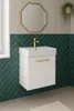 A modern bathroom vanity with a white sink and cabinet, featuring a gold faucet and handle, set against a wall with beige and dark green herringbone tiles. Náhľad obrázku produktu