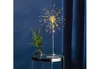 A decorative LED lamp shaped like a firework is displayed on a small table next to a vase of greenery, with a dark blue curtain in the background. Produktbild-Vorschau