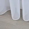 A close-up view of the bottom edge of white sheer curtains resting on a light gray wooden floor. Produktbild-Vorschau