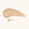A swatch and two drops of liquid foundation on a light beige background. Produktbild-Vorschau