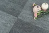 A close-up view of grey carpet tiles with two decorative vases and some pink flowers. Produktbild-Vorschau