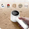 A hand holding a white lint remover device over a brown textured surface, with circular icons of clothing and bedding in the background. Náhled obrázku produktu