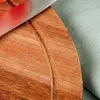 A close-up view of a wooden cutting board with a textured surface, next to a piece of blue fabric. A red and white object is partially visible in the upper left corner. Produktbild-Vorschau