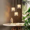 A dining table with three pendant lights hanging above it, set against a backdrop of lush greenery and a textured wall. Produktbild-Vorschau