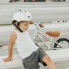 A young child wearing a helmet sits on a bench next to a balance bike. Náhled obrázku produktu