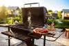 A barbecue grill set up outdoors with food and drinks, ready for a cookout. Produktbild-Vorschau