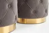 Close-up view of the bottom portion of two gray tufted ottomans with gold bases. Produktbild-Vorschau