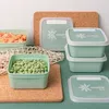 Several green food storage containers are arranged on a cork mat, with some filled with peas and diced carrots. Náhľad obrázku produktu