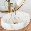 A close-up shot of a marble-patterned sink with a gold faucet. Anteprima dell’immagine prodotto
