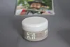 A jar of hair styling cream is placed on a gray surface, with a blurred image of a man in the background. Podgląd zdjęcia produktu