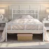 A bedroom scene featuring a white metal bed frame with bedding. Podgląd zdjęcia produktu