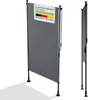 A grey vertical awning or screen is shown standing on a white background with its shadow cast to the left. A small sign with text and the German flag is attached to the top left of the screen. Náhľad obrázku produktu