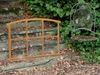 A rusty metal window frame and a metal chair are placed on stone steps outdoors, with lush green foliage in the background. Produktbild-Vorschau