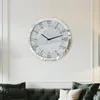 A round wall clock with Roman numerals is mounted on a white wall above a dark green sofa. Podgląd zdjęcia produktu