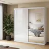 A modern bedroom with a large white sliding door wardrobe with mirrored doors, reflecting a bed and a framed picture on the wall. A large potted plant is placed next to the wardrobe. Produktbild-Vorschau