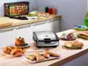 A kitchen counter with a waffle maker, various snacks, and ingredients. Voir les images du produit