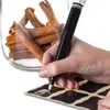 A hand is writing on a label with a marker, with a jar of cinnamon sticks in the background. Produktbild-Vorschau
