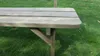 A close-up view of a wooden picnic table bench, with grass in the background. Produktbild-Vorschau